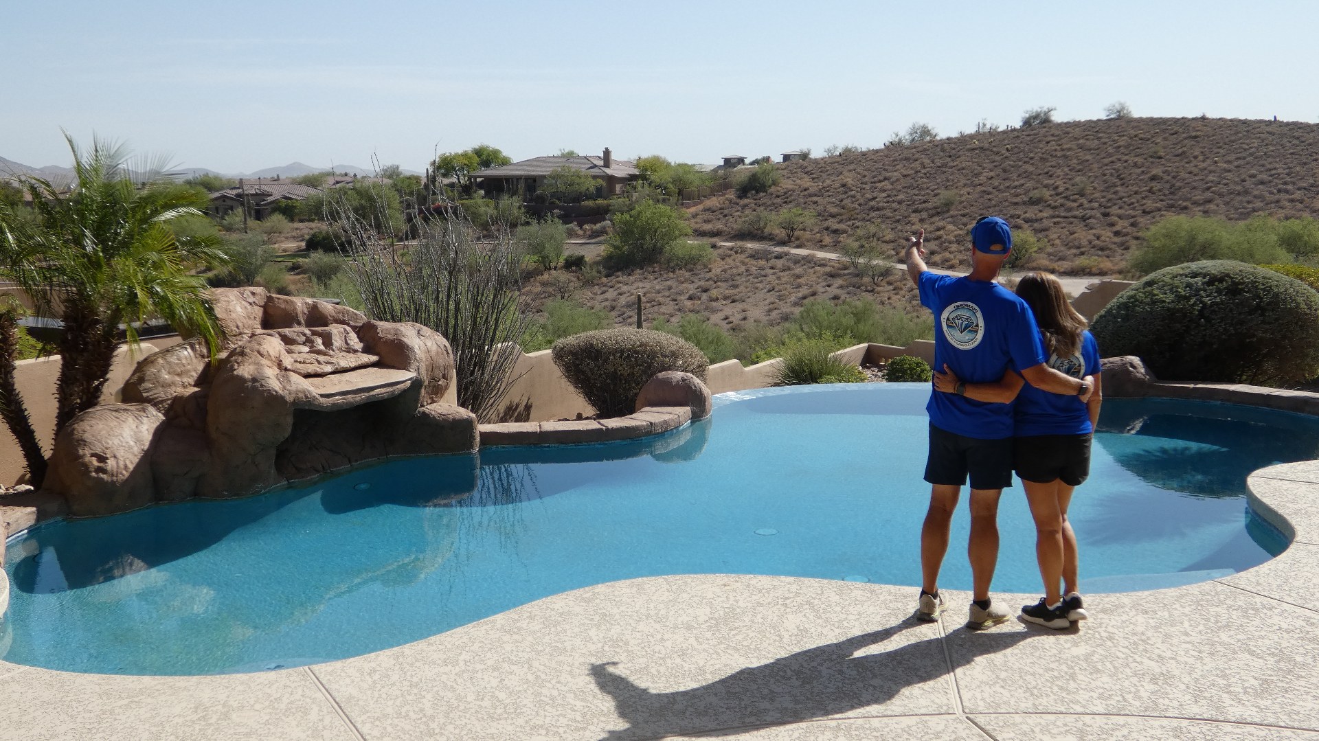 Brian and Sherry, owners of Diamond Pool Cleaning, standing arm-in-arm at the edge of a sparkling Cave Creek backyard pool overlooking the desert.